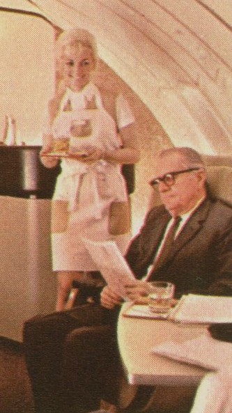 1970 A Flight Attendant wearing an apron to match her Galaxy Gold uniform serves customers in a mock up of a 747 upper deck lounge.
